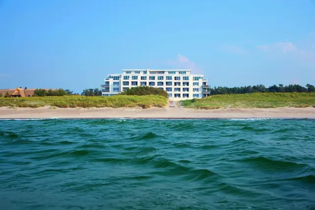 The reed-thatched houses of Strandhotel Dünenmeer from above, with the Baltic Sea and the dune forest running north
